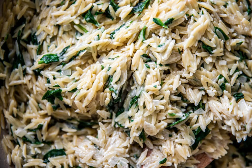 A close up of large pot of creamy parmesan orzo with lots of spinach.  
