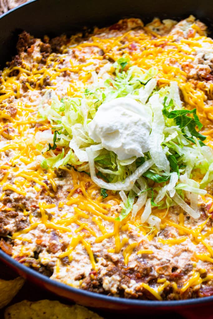 a cast iron skillet on a table.  In the skillet is ground beef, cheese, and salsa topped with shredded lettuce and sour cream.  