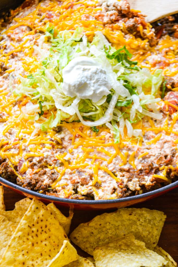 a cast iron skillet on a table.  In the skillet is ground beef, cheese, and salsa topped with shredded lettuce and sour cream.  There are chips on the bottom of the skillet to serve.